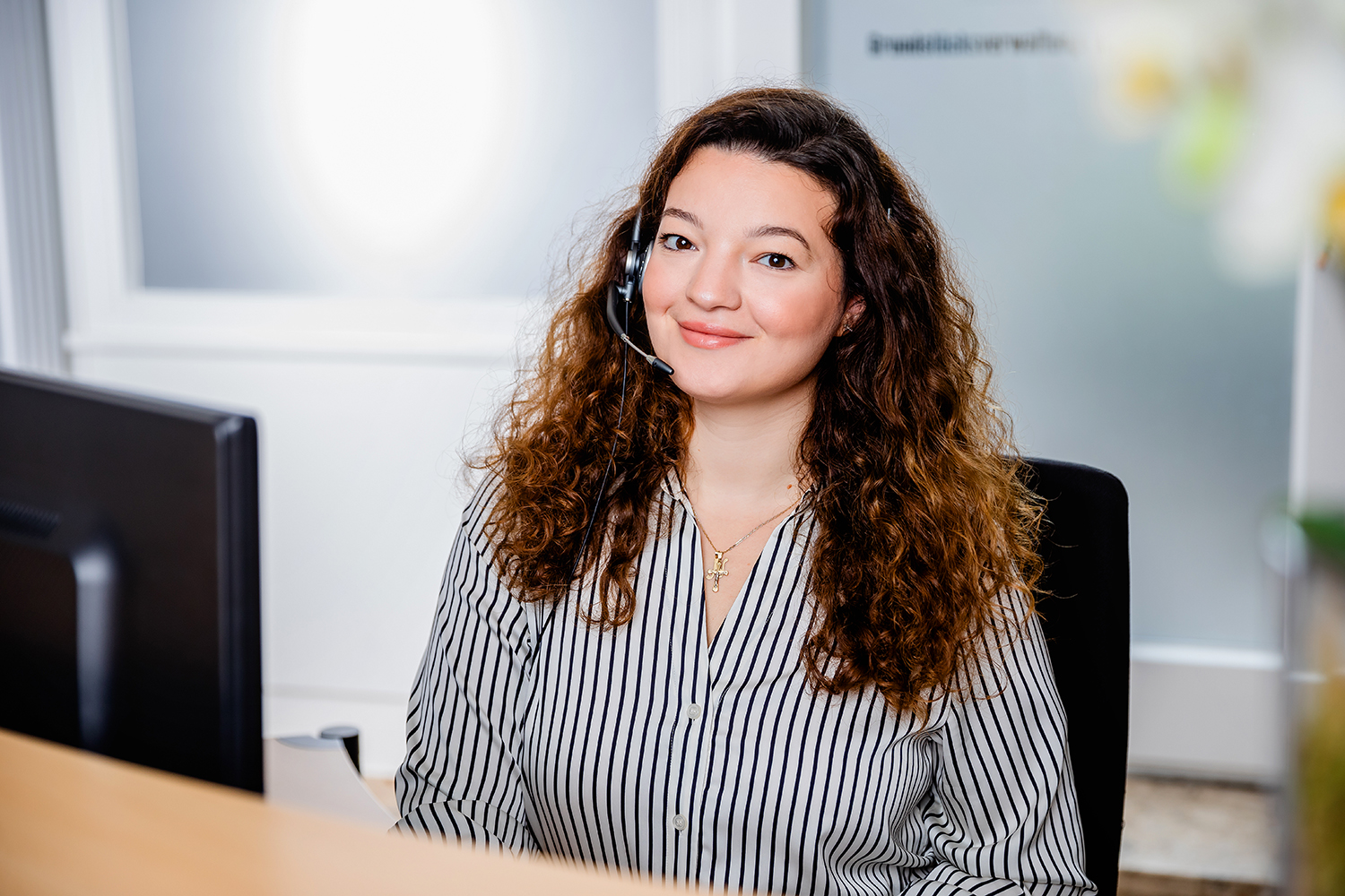 Portrait der Mitarbeiterin Njomza Cubi, sie sitzt am Schreibtisch und lächelt in die Kamera